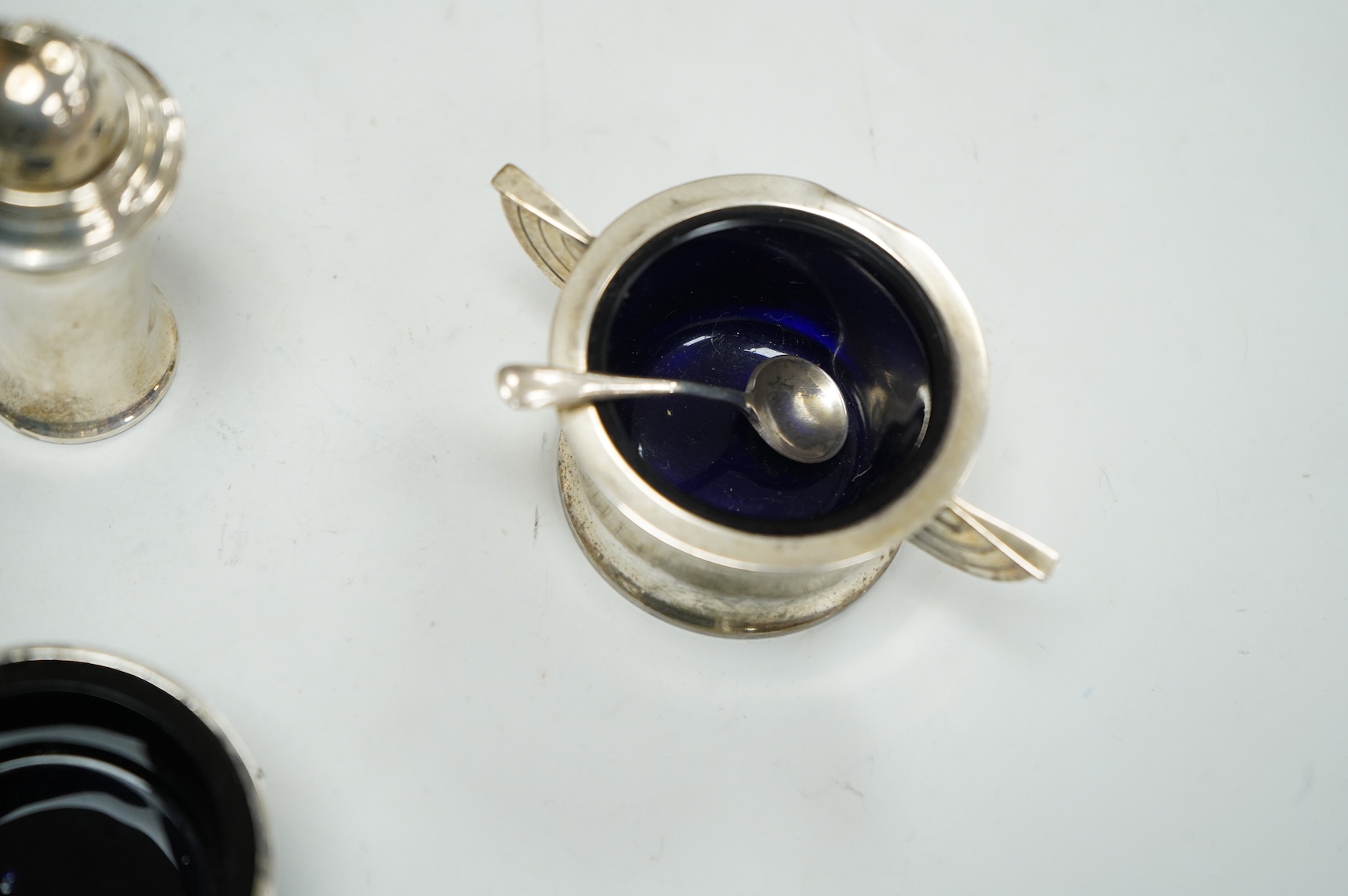 A George V Art Deco three piece silver condiment set and two spoons by William Adams Ltd, Birmingham, 1935, together with a pair of late Victorian pierced silver salts with blue glass liners and an Edwardian silver musta